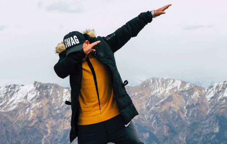 A man in a parka and ball cap reading Swag does "The Dab" move