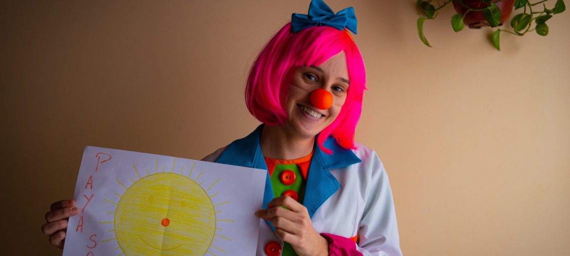 A woman dressed as a clown holds a large piece of paper