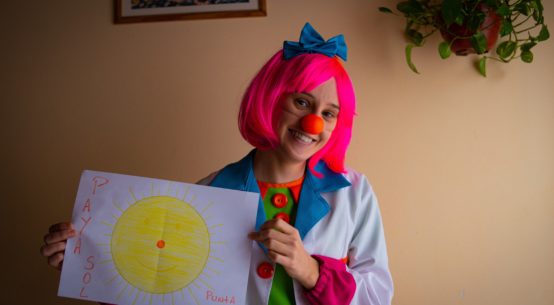 A woman dressed as a clown holds a large piece of paper