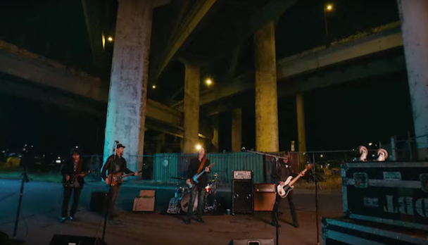 The Drive By Truckers stand beneath a freeway overpass playing their instruments