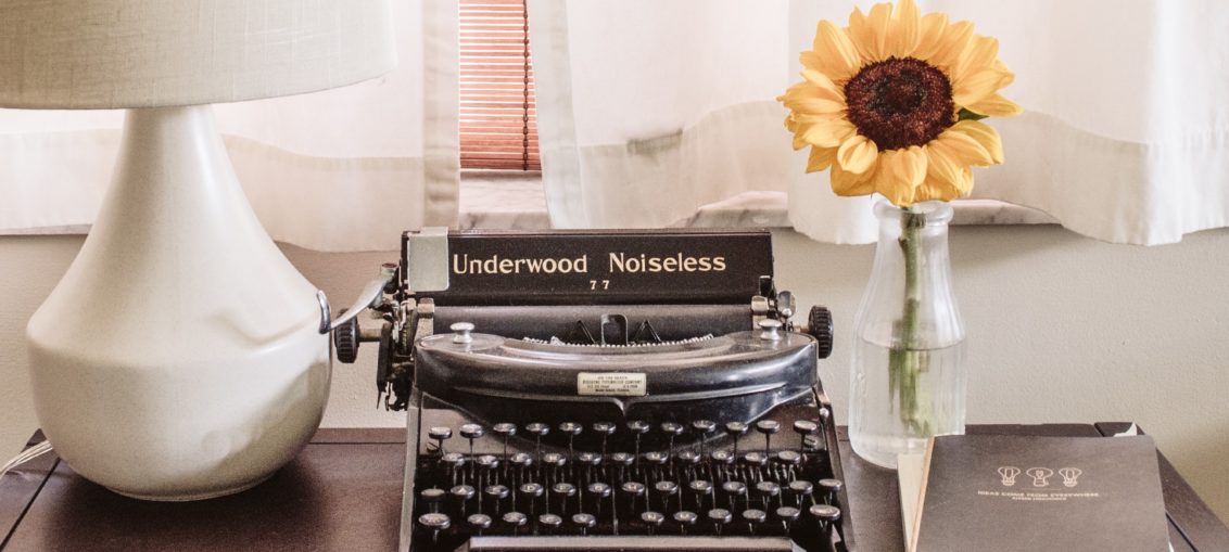 typewriter on desk with lamp and sunflower in a vase and a file of papers