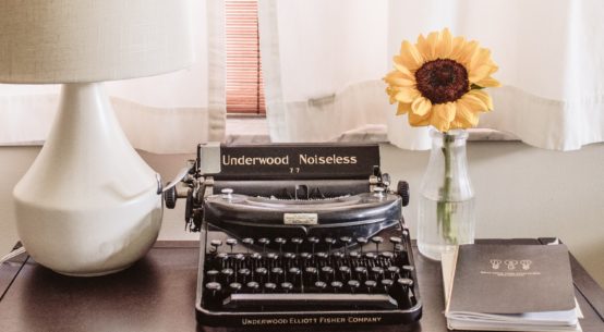 typewriter on desk with lamp and sunflower in a vase and a file of papers