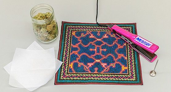 A jar of cannabis buds sits next to a hair straightening iron and some parchment paper
