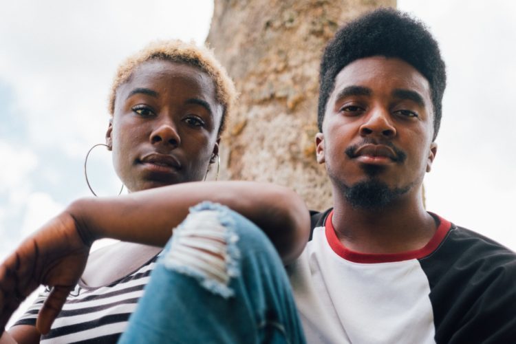 A black man and woman sit in front of a tree facing the camera