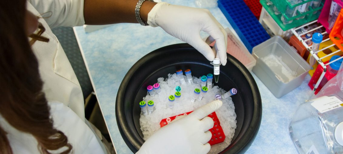 A black female lab staff member is sorting through some samples in liquids in test tubes submerged in a bowl filled with ice