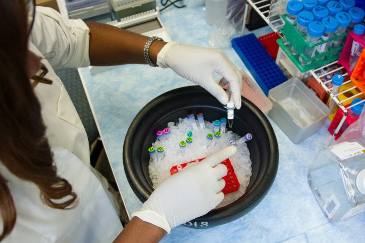 A black female lab staff member is sorting through some samples in liquids in test tubes submerged in a bowl filled with ice