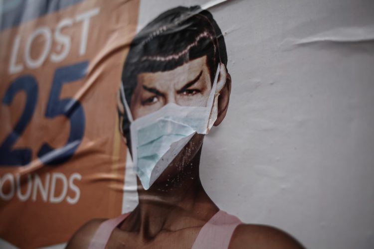 A mural of the character Spock from Star Trek has a surgical mask someone has attached which is fluttering in the breeze.