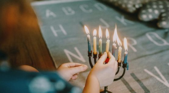 a hand lights the final candle of a Menorah