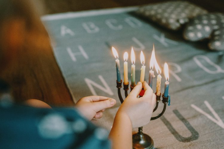 a hand lights the final candle of a Menorah