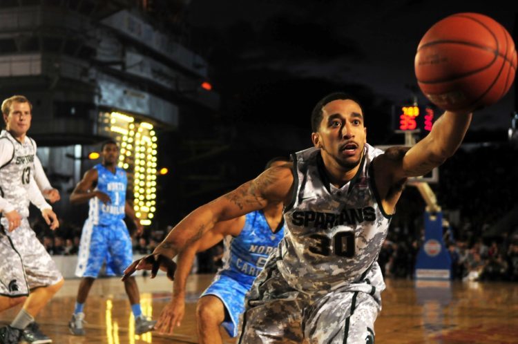 A man playing a college basketball game reaches for the ball