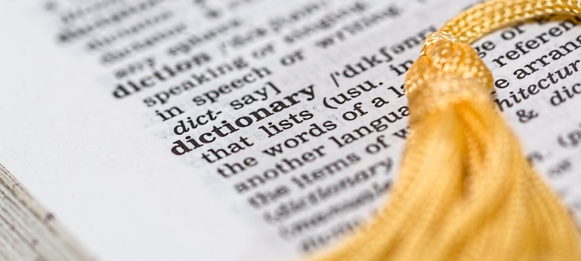 A dictionary is open to the word dictionary, with a yellow tassel bookmark laying across the page