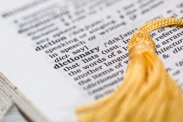 A dictionary is open to the word dictionary, with a yellow tassel bookmark laying across the page