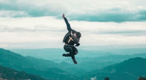 A man jumps and does "the Dab" high above a city